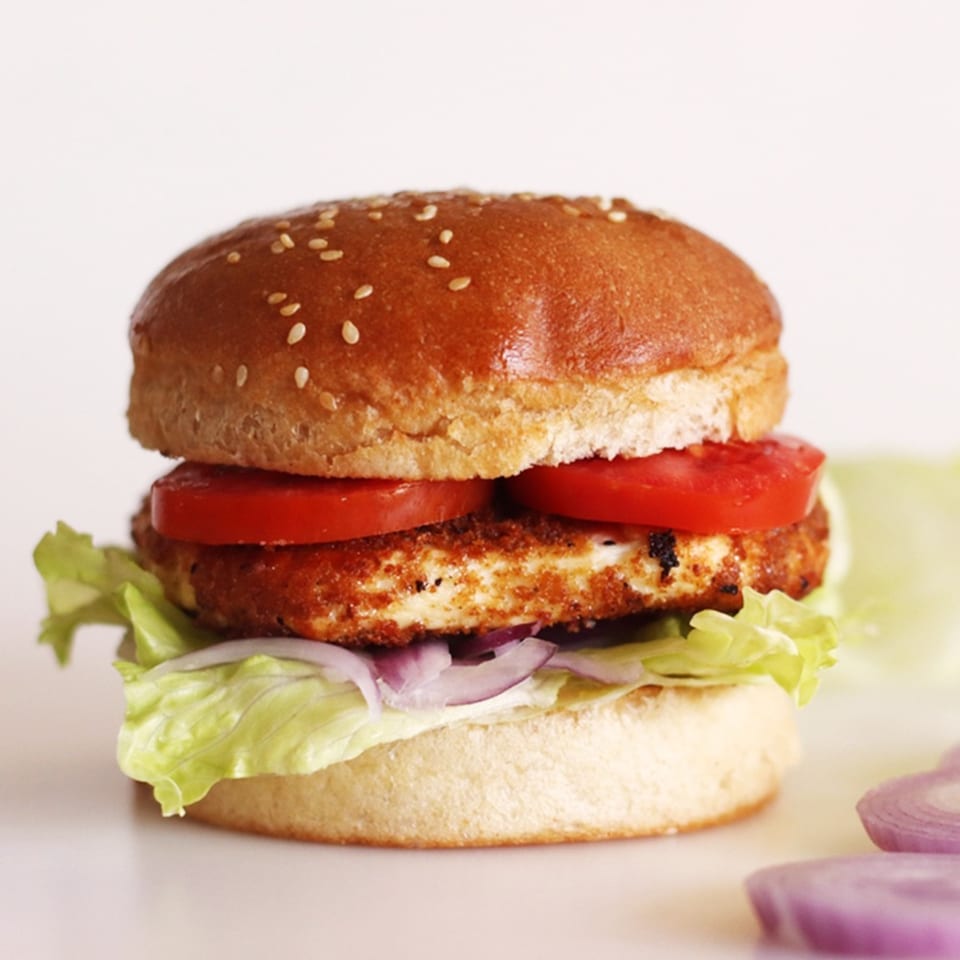 Vegetarian burger with a sesame bun, grilled patty, sliced tomatoes, lettuce, and red onion on a light background.