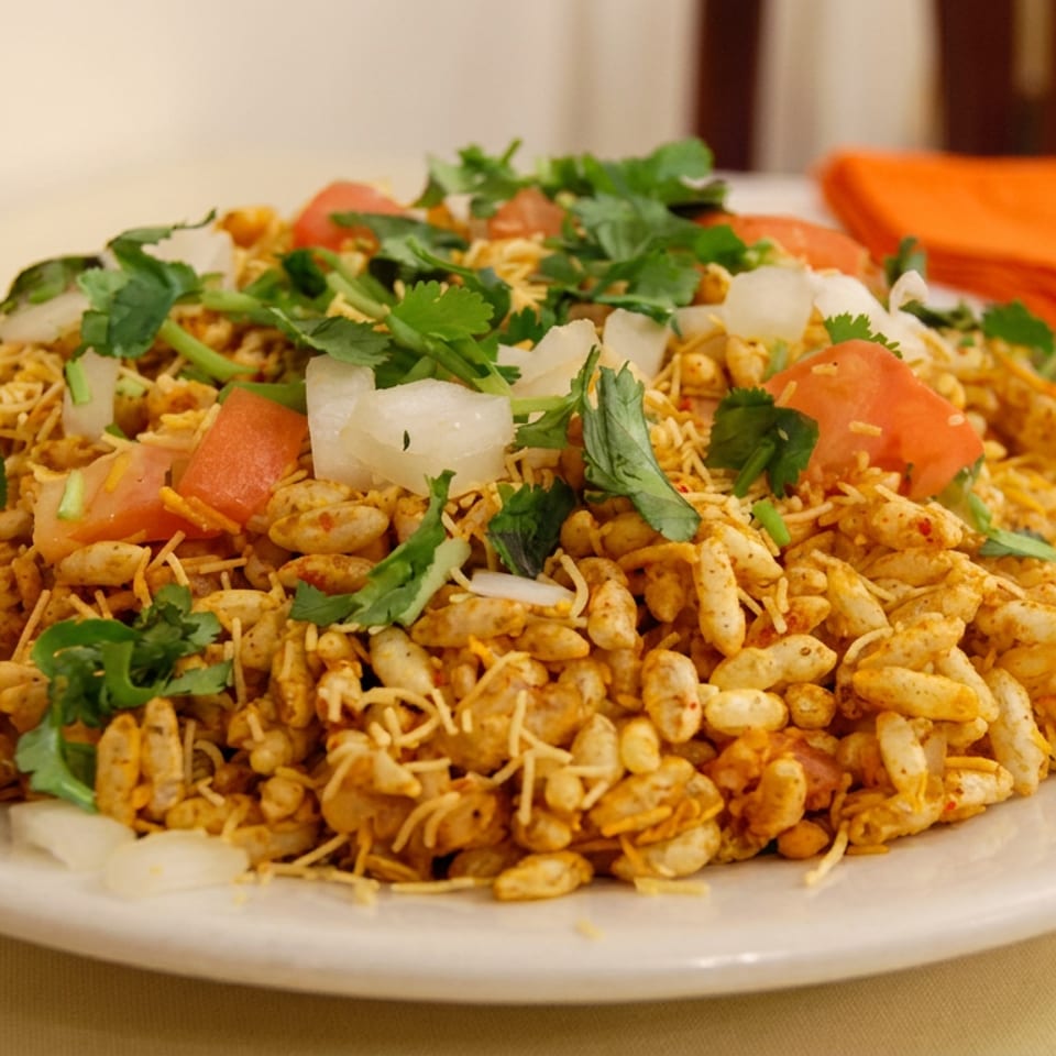 Plate of Indian bhel puri topped with puffed rice, sev, tomatoes, onions, and fresh cilantro.